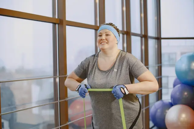 A smiling woman using a resistance band for a workout in a gym.