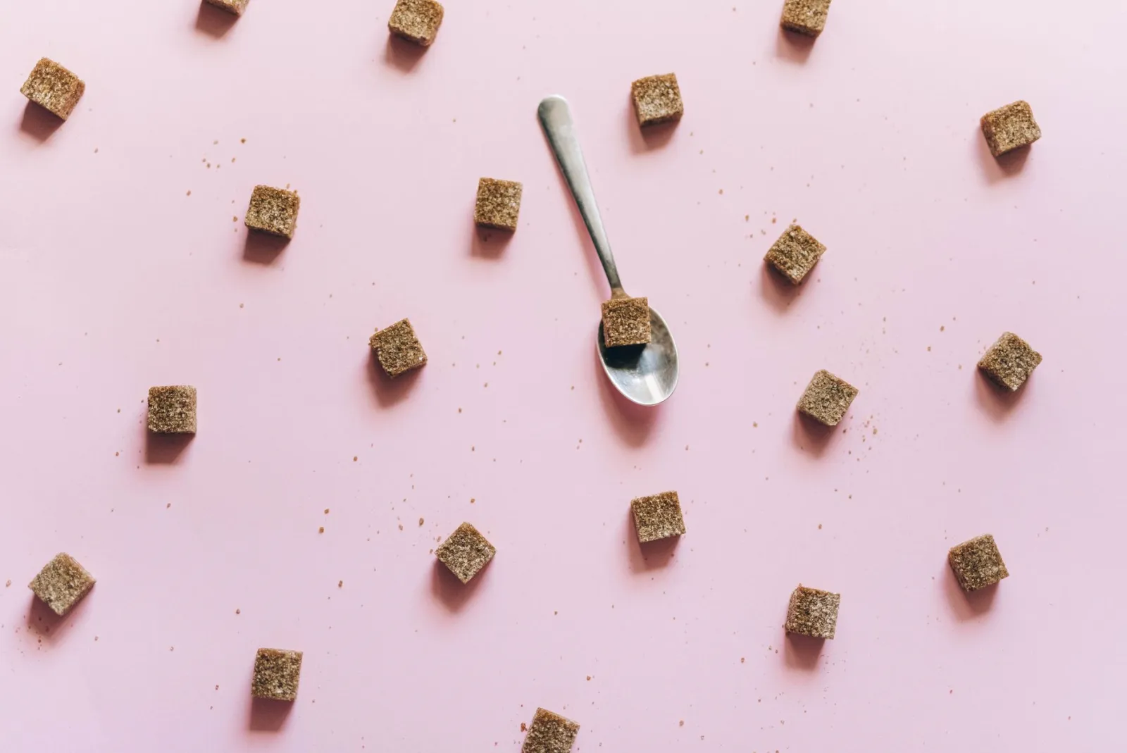 Brown sugar cubes scattered across a plain coloured surface, seen from above.