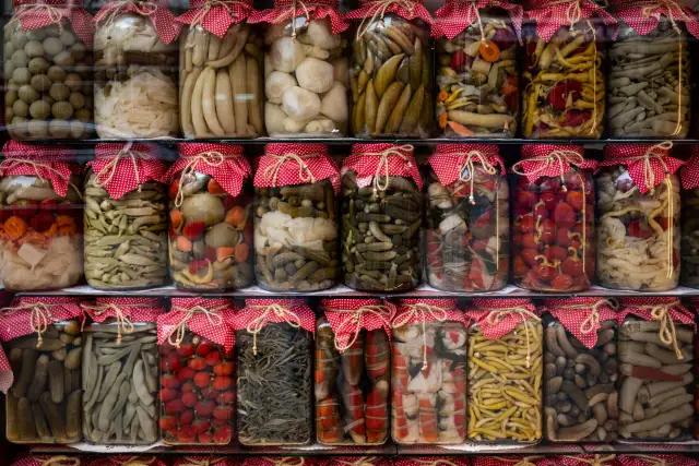 An assortment of pickled vegetables in glass jars with cloth covers on a table.
