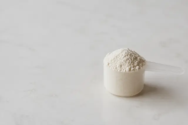 A plain measuring scoop of white powder on a neutral surface in soft daylight.