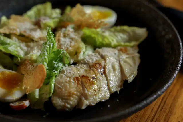A plated meal of grilled chicken, mixed greens, and a boiled egg on a kitchen counter.