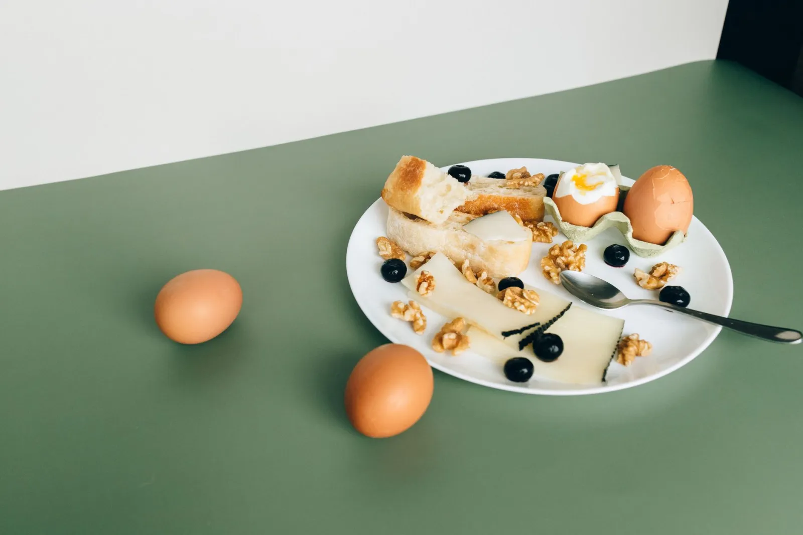 A plate of cheese, boiled eggs, bread, walnuts, and blueberries.