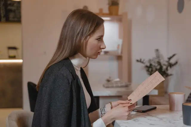 Side view of woman holding menu in a cozy café setting, wearing a turtleneck and jacket.
