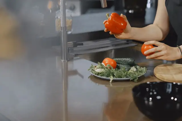 A person slicing fresh vegetables on a cutting board in a bright kitchen.