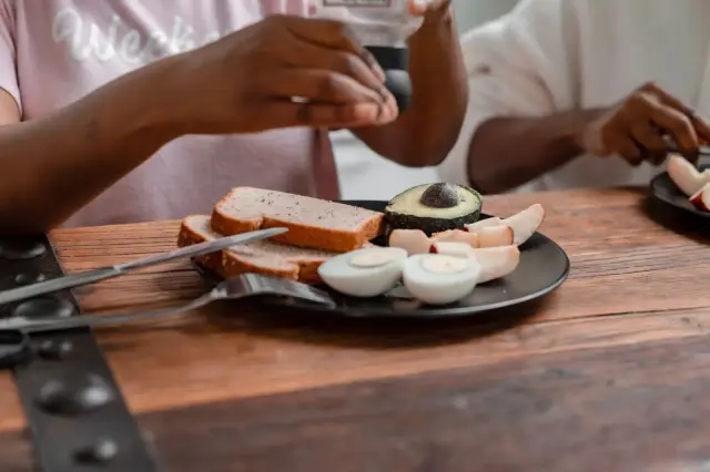 A breakfast plate with avocado, boiled eggs, and bread on a wooden table.