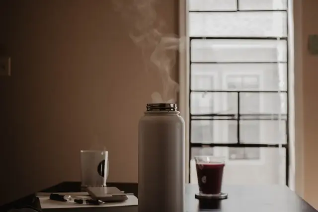 A woman sipping a warm drink by a window in soft morning light.