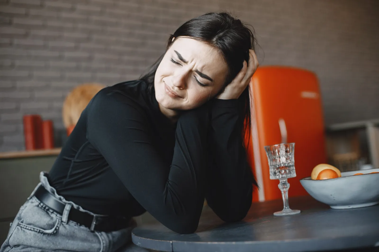 A woman sitting alone at a dinner table in low evening light, looking tense.
