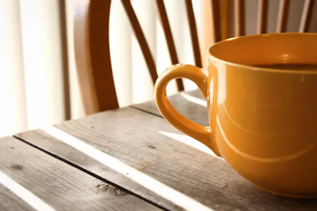 A warm mug of coffee on a wooden table in soft morning light, the quiet after food noise fades.