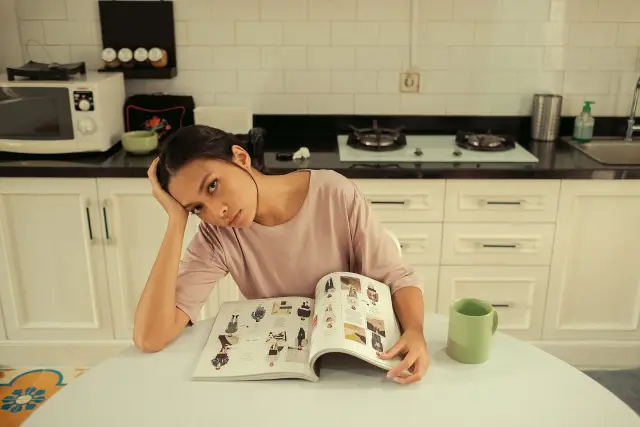 A woman sitting on a sofa, looking away from a bowl of food beside her.
