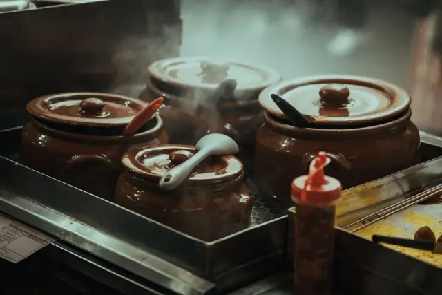Steaming traditional clay pots with utensils on a stove in a home kitchen.