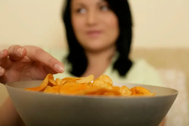 A woman reaching for a bowl of potato chips in a home kitchen.