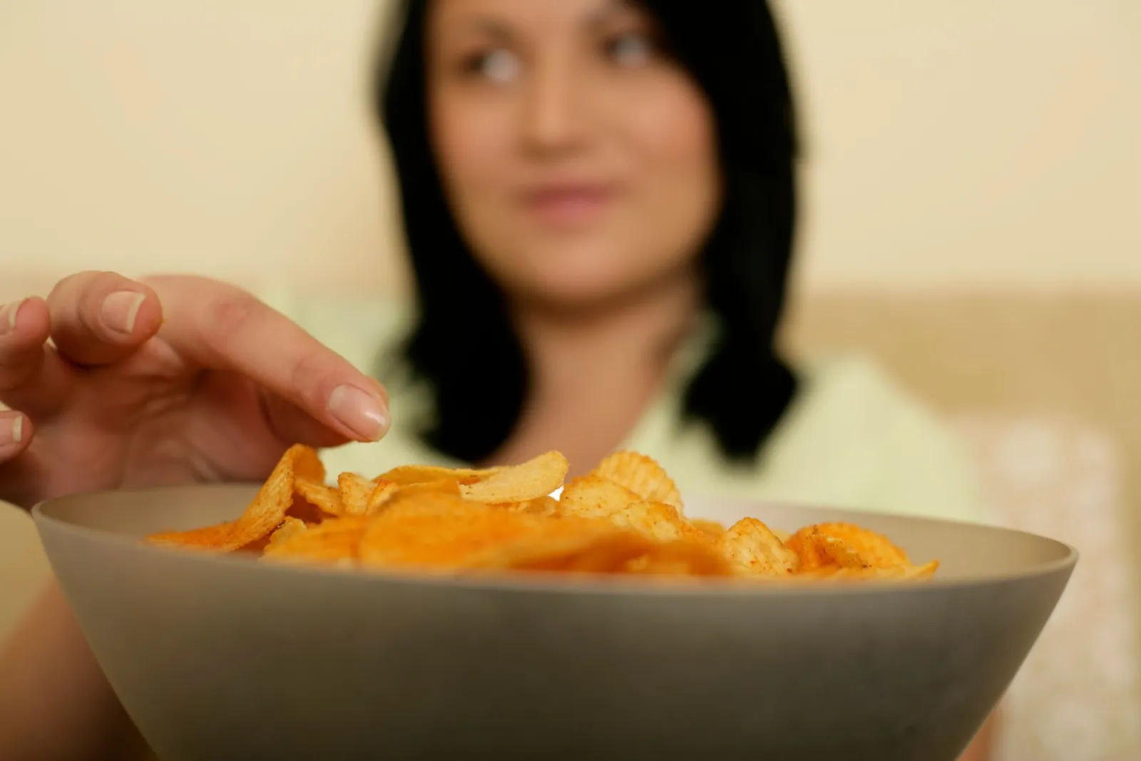 A woman reaching for a bowl of potato chips in a home kitchen.