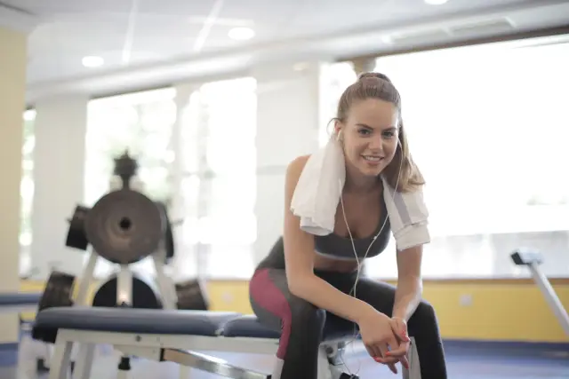 A woman taking a break on a gym bench with a towel and headphones.