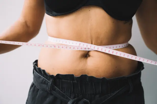 A person measuring their waist with a tape measure.