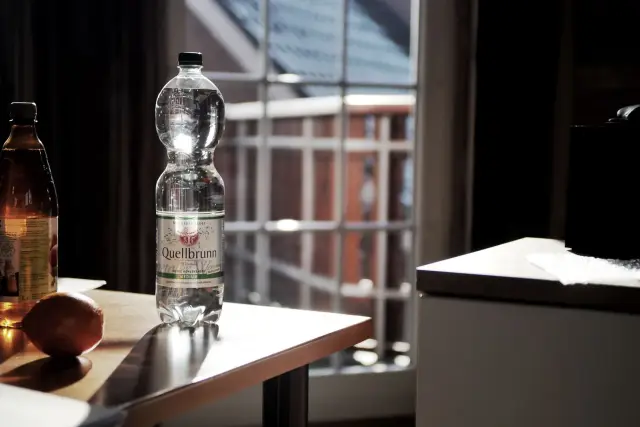 A bottle of water on a table beside a bright window.