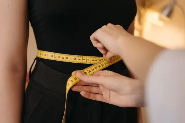 A tape measure held around a waist, cropped close, on a plain background.