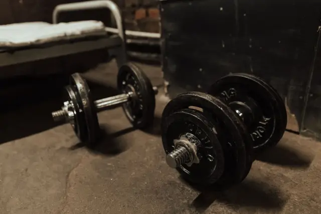 A pair of dumbbells resting unused on a concrete floor in dim indoor light.