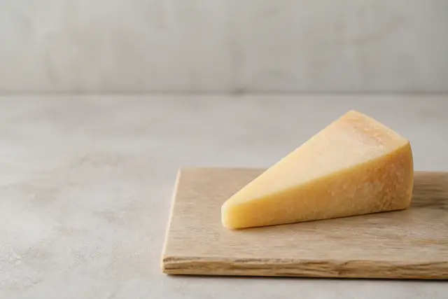 A wedge of hard cheese on a plain wooden board in soft daylight.