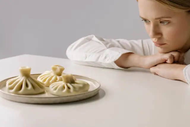 A woman seated alone at a dinner table, gazing at a plate of food without eating.