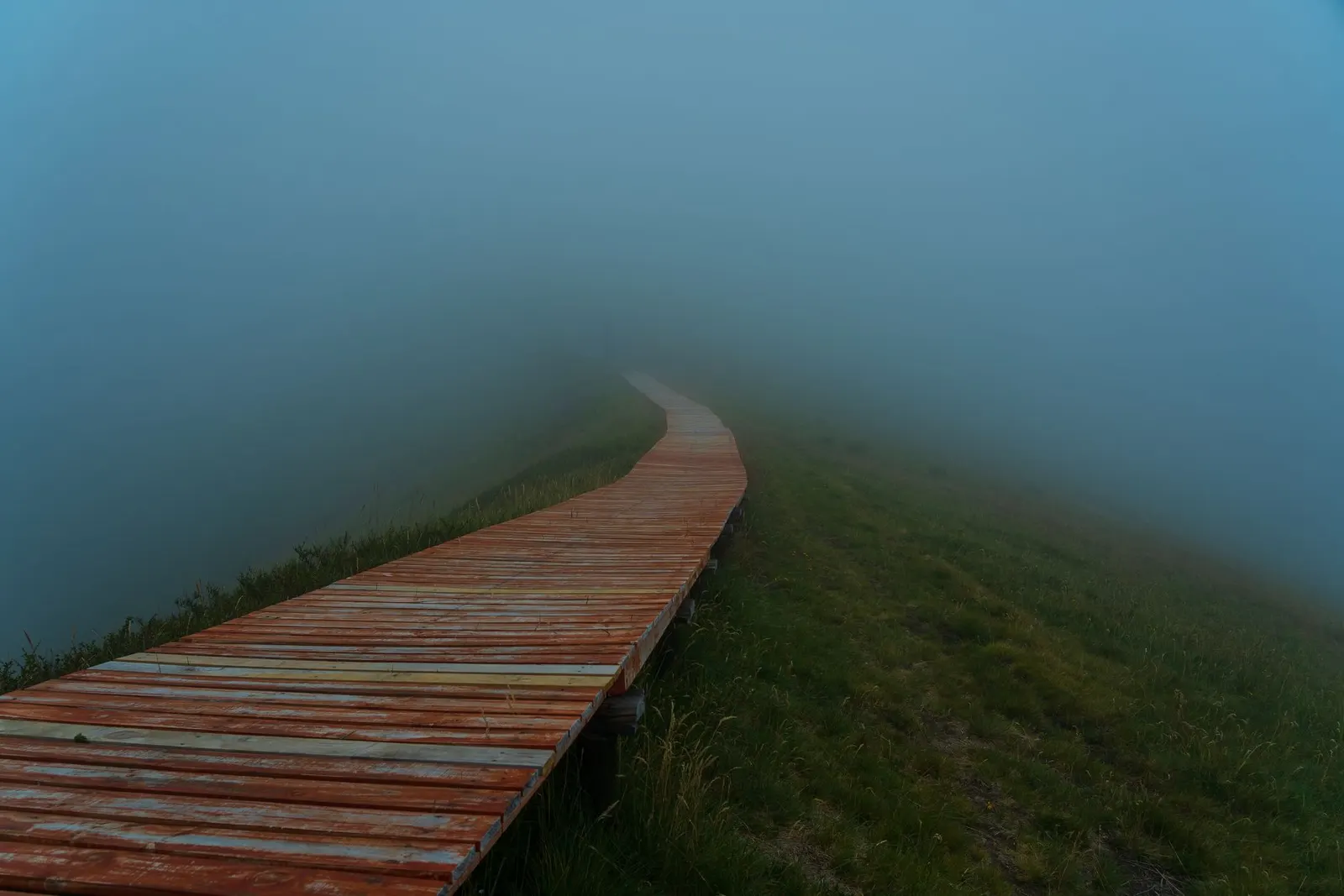 A woman in an orange jacket hiking on a foggy mountain day.