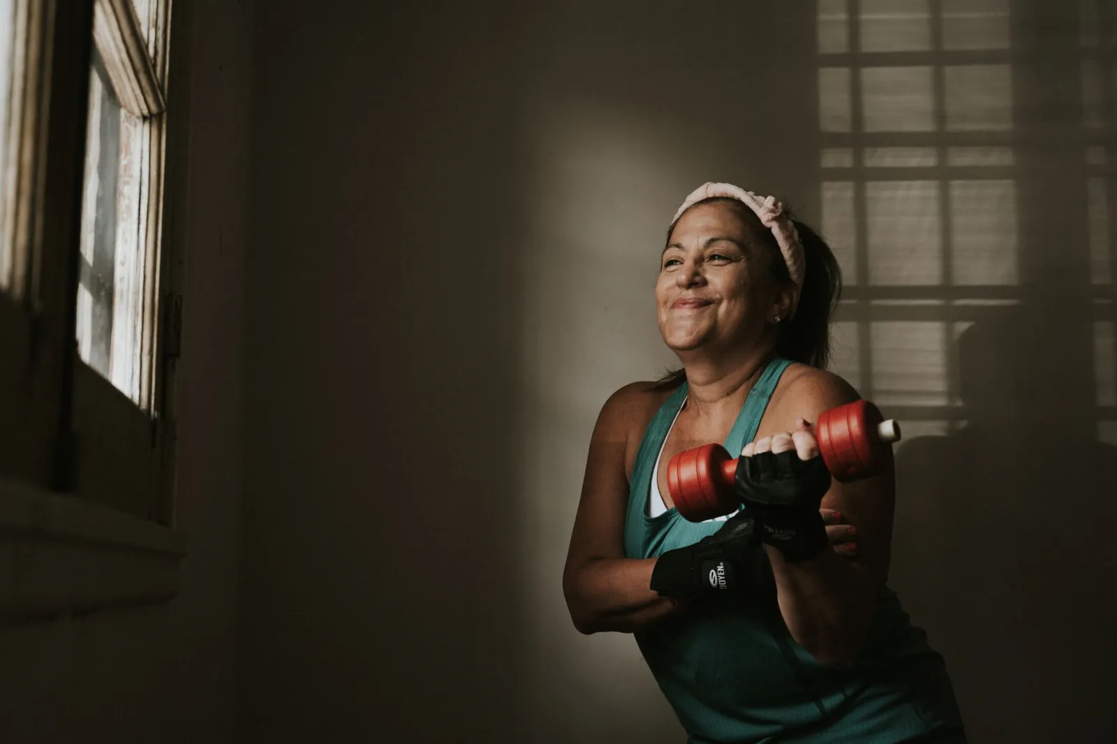 Confident middle-aged woman lifting dumbbells indoors, embracing a healthy lifestyle.